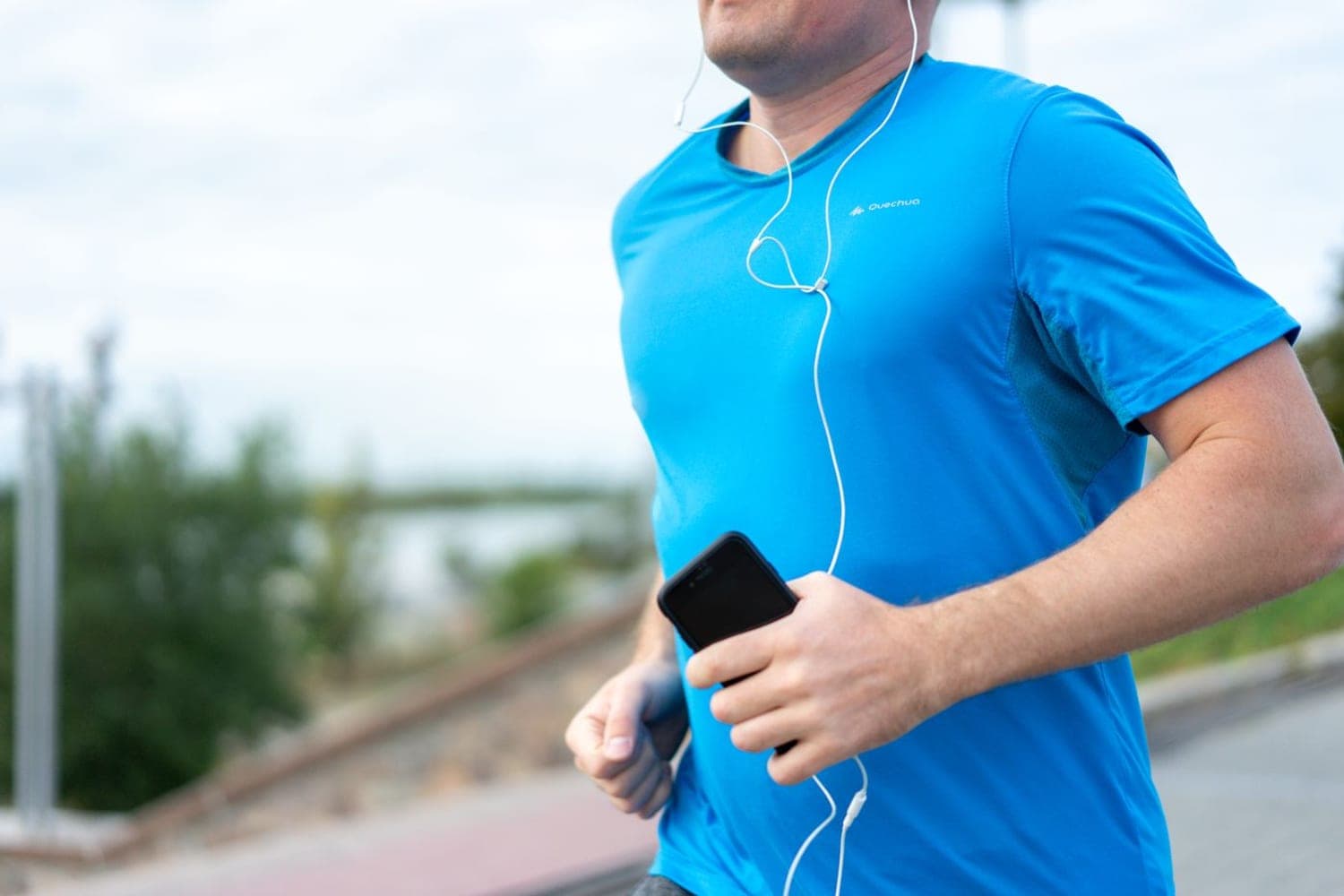 Biegacz w koszulce sportowej trzyma w dłoni telefon podczas treningu